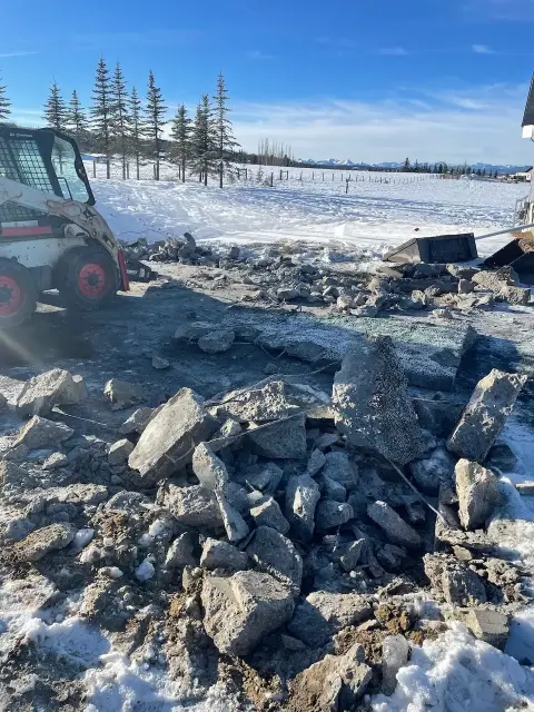 Demolition services clearing a snow-covered area of large rocks and debris