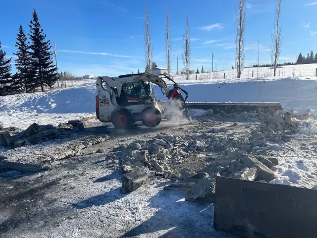 Demolition services using a skid steer to clear rubble from a snowy construction site