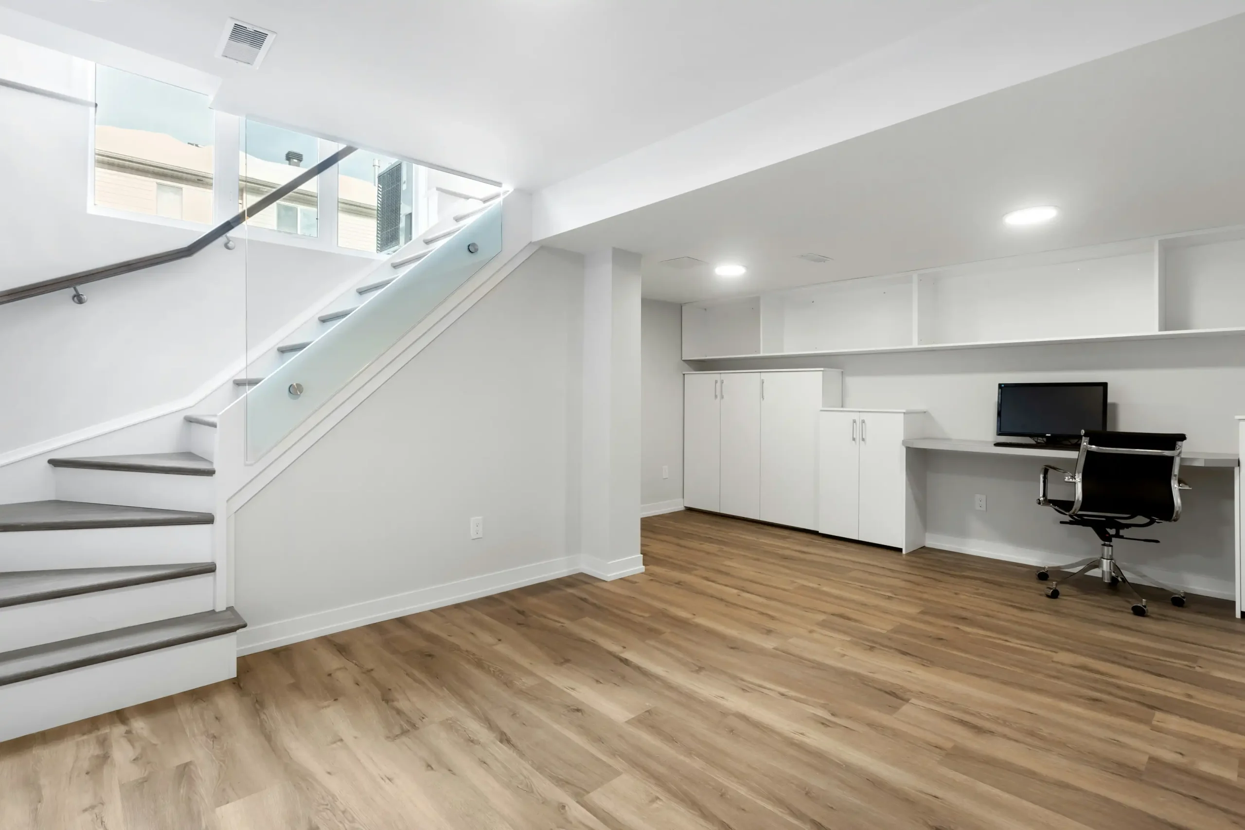 Modern basement renovations in Calgary feature a bright, spacious room with wooden flooring and a stylish desk