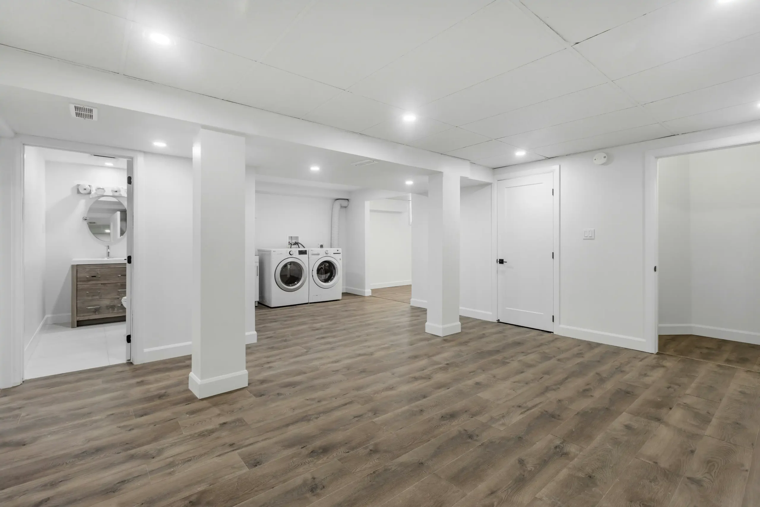 Bright basement renovations in Calgary showcase laundry appliances and light wood flooring